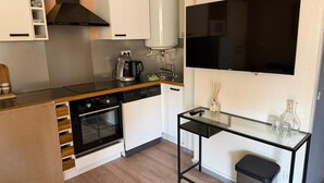A compact kitchen with a built-in oven, a coffee maker, a water dispenser, and a flat-screen TV mounted on the wall. - Modern Beach Apartment Valras (Valras-Plage)