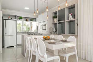 A modern kitchen with white cabinetry, a central island, and pendant lighting. - Elegante Casa com Piscina - Canasvieiras (Florianópolis)