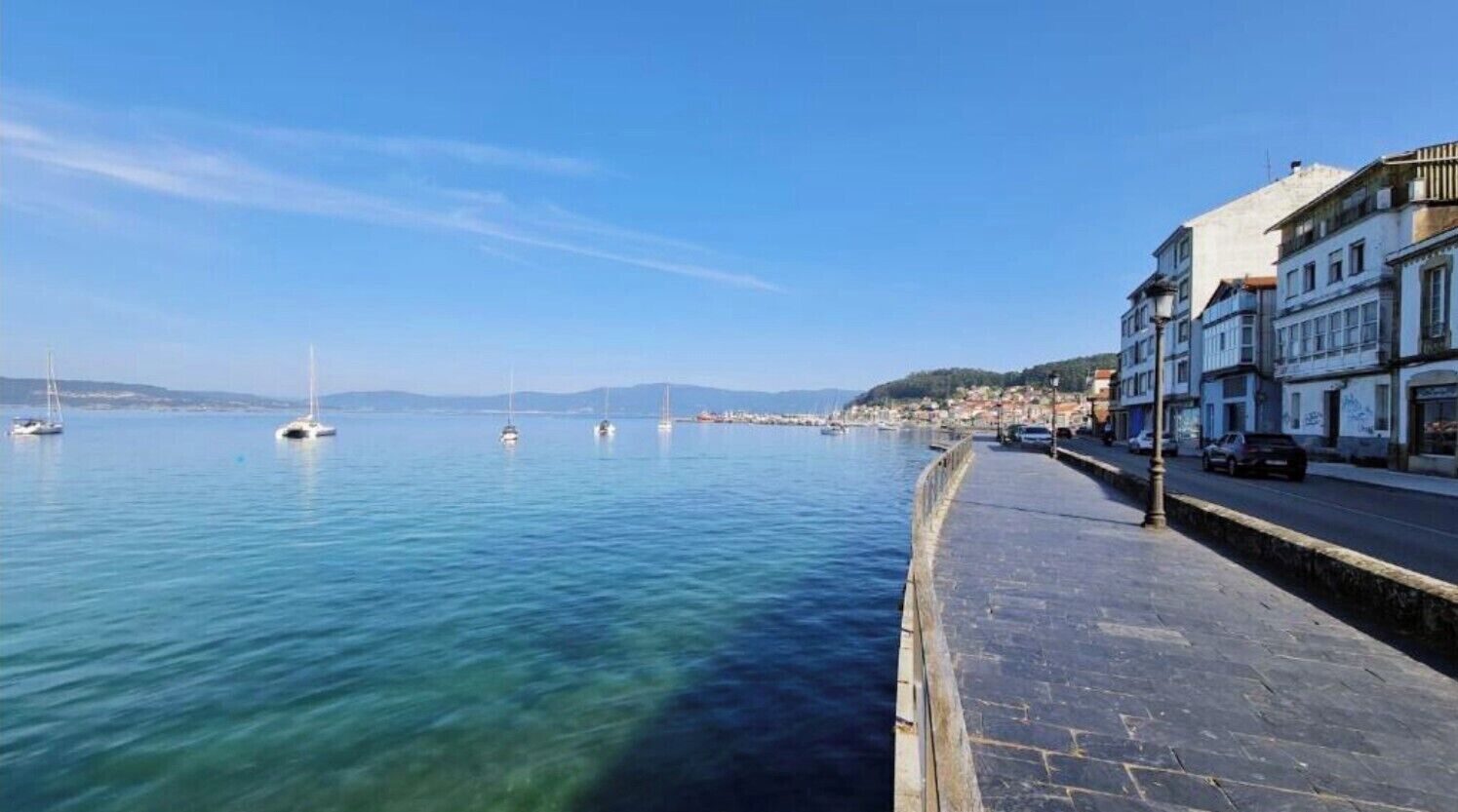 Une promenade en bord de mer, bordée d’immeubles, avec un ciel dégagé et des bateaux sur l’eau.