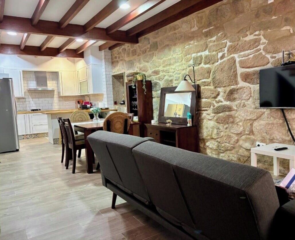 A cozy living area with a stone wall, a sofa, a television, and a kitchen in the background.