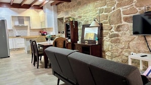 Un salon chaleureux avec un mur en pierre, un canapé, un téléviseur et une cuisine en arrière-plan.