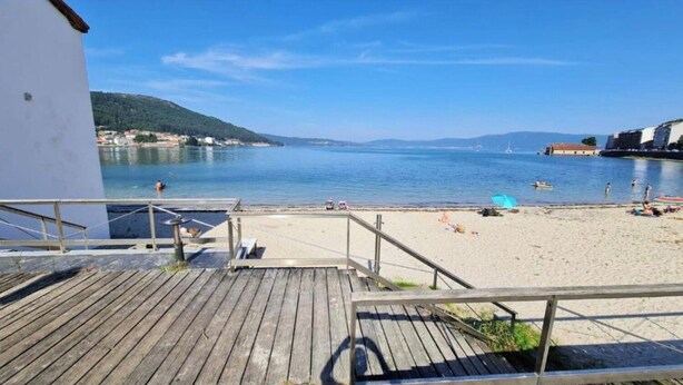 Une terrasse en bois qui mène à une plage, offrant une vue dégagée sur la mer et les collines lointaines.