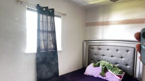 Ein Zimmer mit Bett, einem Fenster mit Vorhang, einem Deckenventilator und einer dekorativen Wandbordüre.