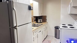 Eine kleine Küche mit Kühlschrank, Spüle, Herd und Kaffeemaschine.