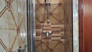 Un box de ducha con puerta de vidrio, un cabezal de ducha de mano y otro cabezal de ducha con manguera.