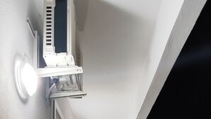 Un estrecho pasillo con una unidad de aire acondicionado en el techo, una puerta con manija y una ventana en la pared derecha.
