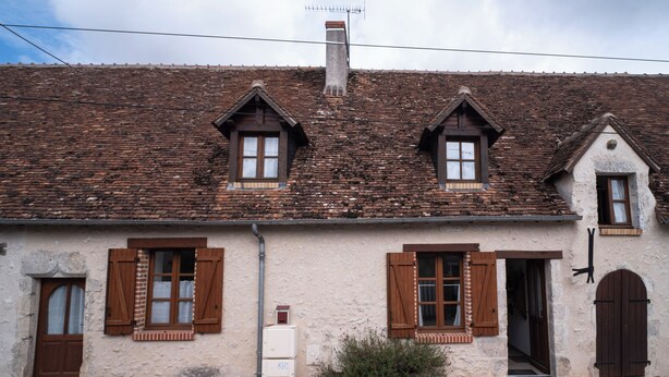 A traditional building with a tiled roof, wooden shutters, and a small chimney.