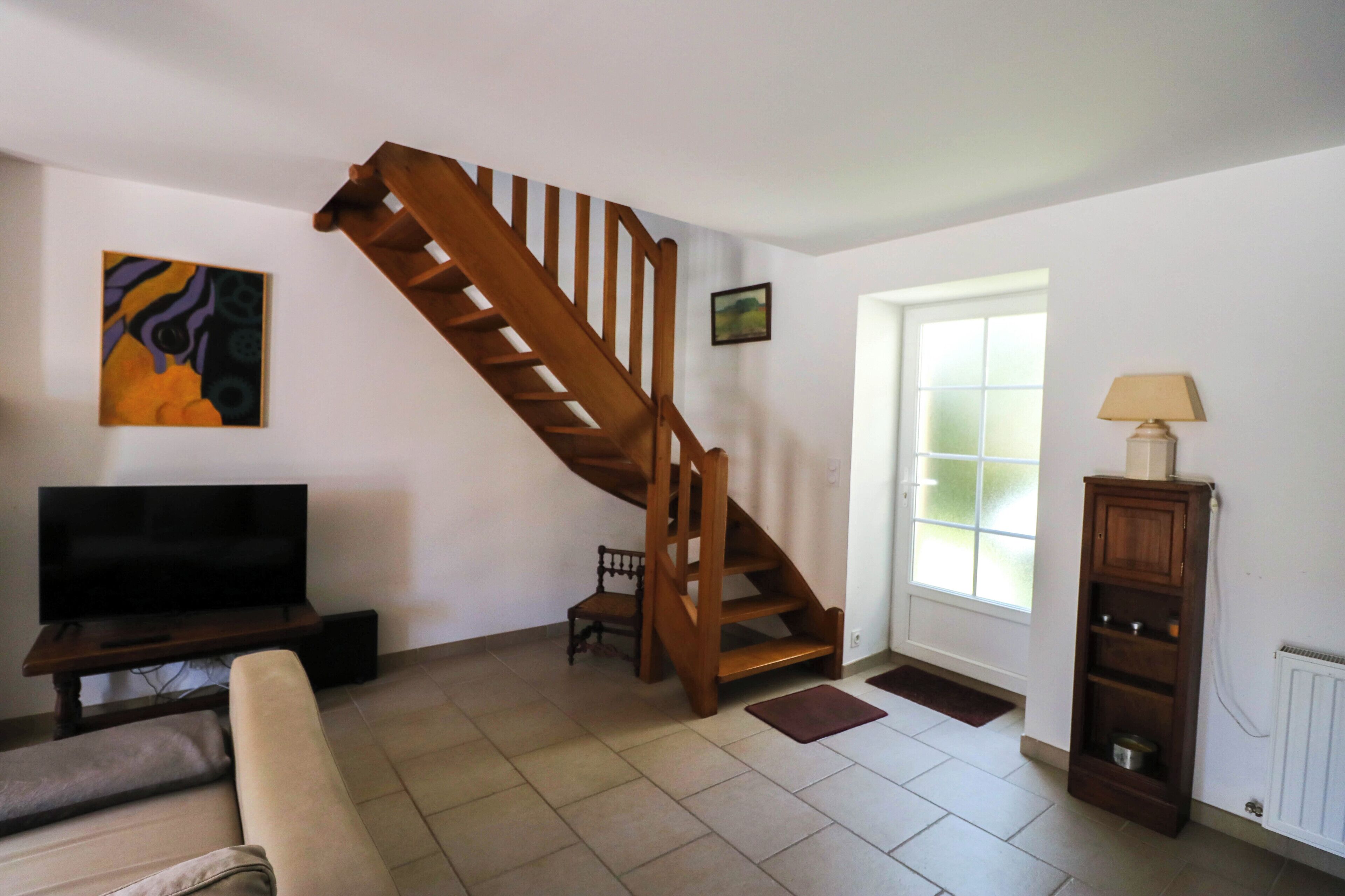 A living room with a wooden staircase, a television, a sofa, a lamp, and a window.