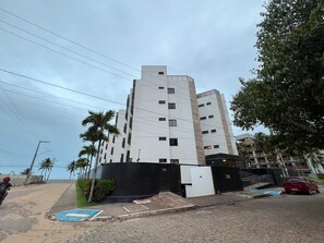 Ein mehrstöckiges Gebäude mit modernem architektonischen Design, ein markanter Eingang mit schwarzem Tor und ein sichtbarer Parkbereich.