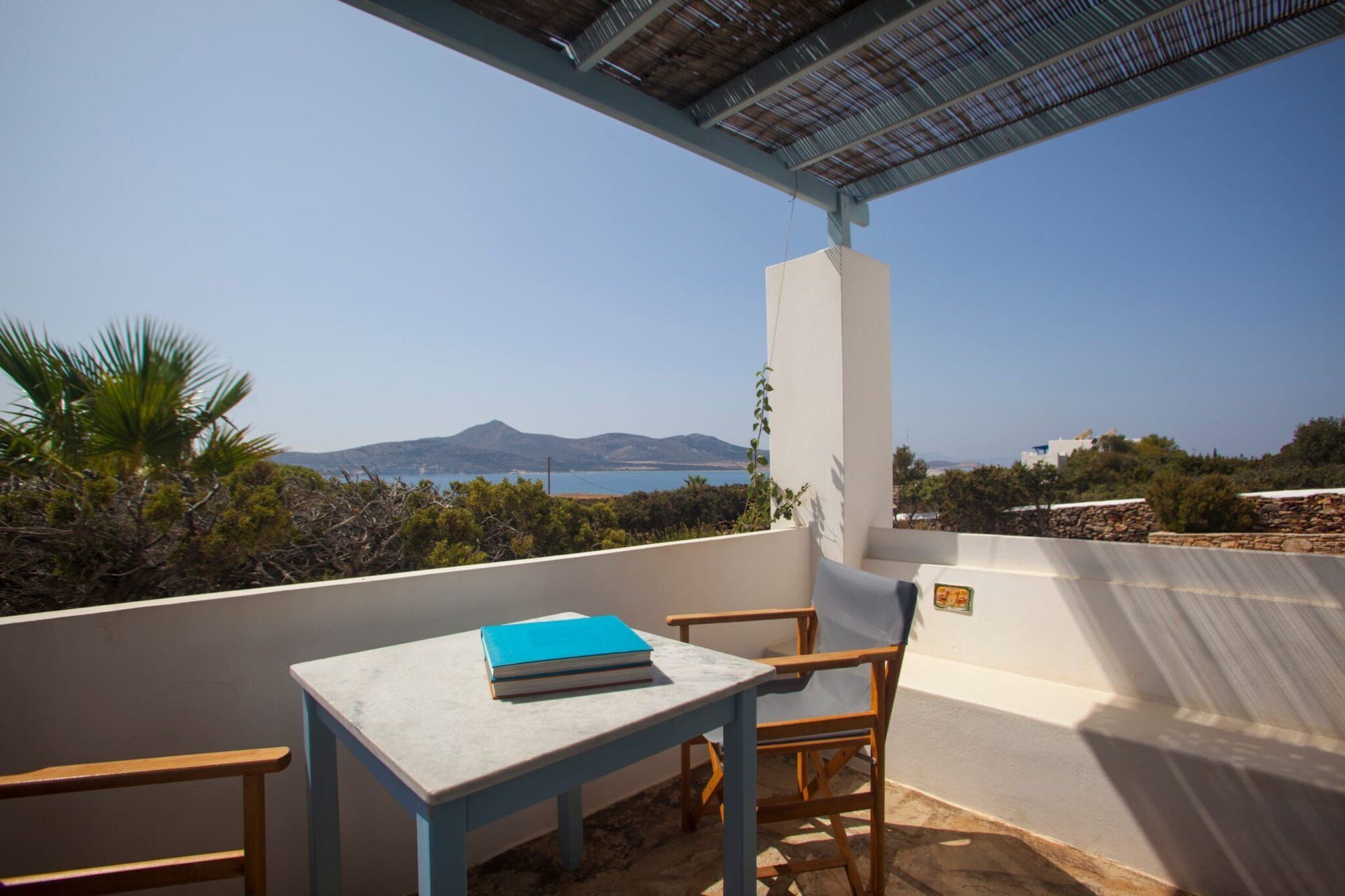En balkon med et bord og stole, der giver udsigt over et smukt landskab med bjerge og hav.