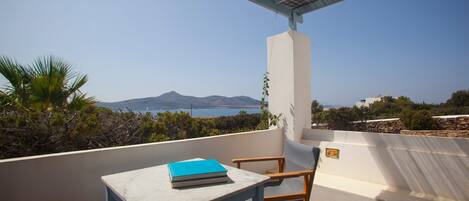 En balkon med et bord og stole, der giver udsigt over et smukt landskab med bjerge og hav.