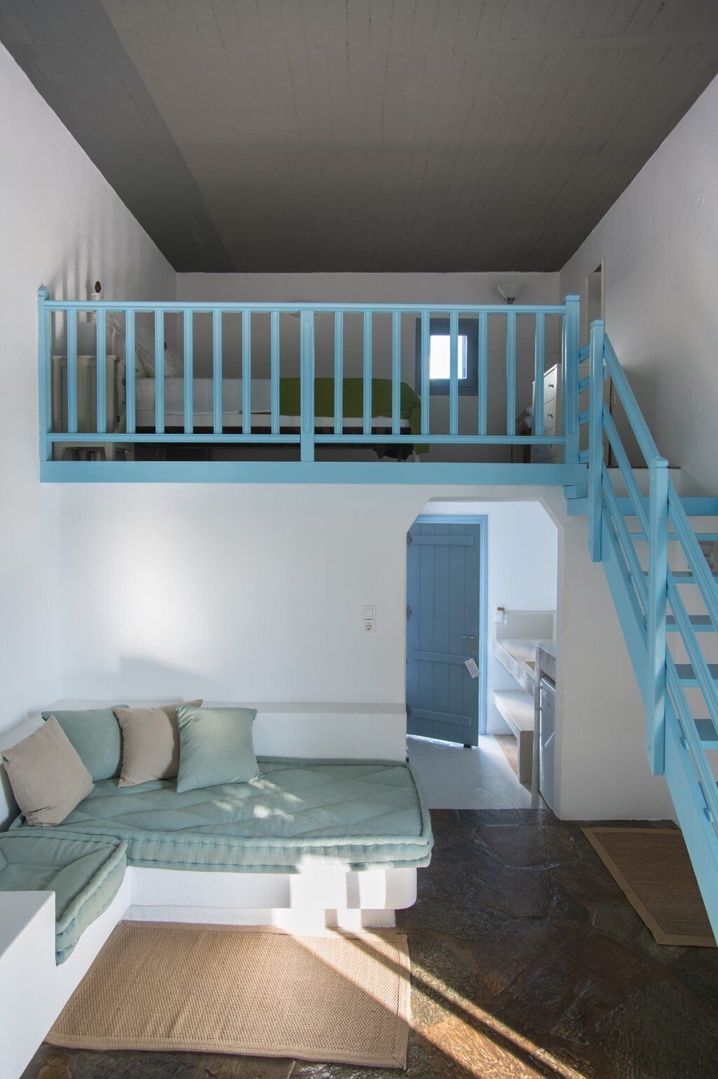 A loft bedroom with a bunk bed, a sofa bed, a staircase, and a door leading to another room.