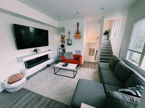 Ein modernes Wohnzimmer mit Flachbildfernseher, einem roten Sofa, einem grauen Couchen, einem Couchtisch und einer Treppe, die in eine andere Ebene führt.