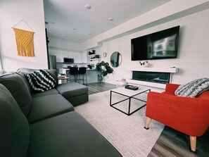 Ein modernes Wohnzimmer mit einem grauen Ecksofa, einem roten Sessel, einem Couchtisch und einem flachbildfernseher, der an der Wand montiert ist.