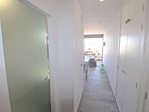 A hallway with a door on the left, a bed with a nightstand and lamp in the center, and a wardrobe on the right. - ESTUDIO PLAYA MUCHAVISTA by Interhome (El Campello/Villajoyosa)