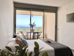 A bedroom with a bed, a bedside table, a chair, and a view of the sea through a large sliding door. - ESTUDIO PLAYA MUCHAVISTA by Interhome (El Campello/Villajoyosa)