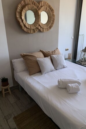 A neatly made bed with white linens, two large circular wall mirrors, and a small potted plant on a wooden stool. - ESTUDIO PLAYA MUCHAVISTA by Interhome (El Campello/Villajoyosa)