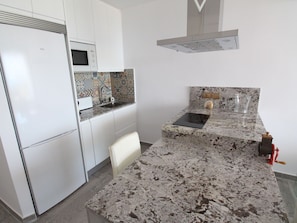 A kitchen with white cabinets, a built-in microwave, a patterned backsplash, a granite countertop, and a red kitchen tool. - ESTUDIO PLAYA MUCHAVISTA by Interhome (El Campello/Villajoyosa)