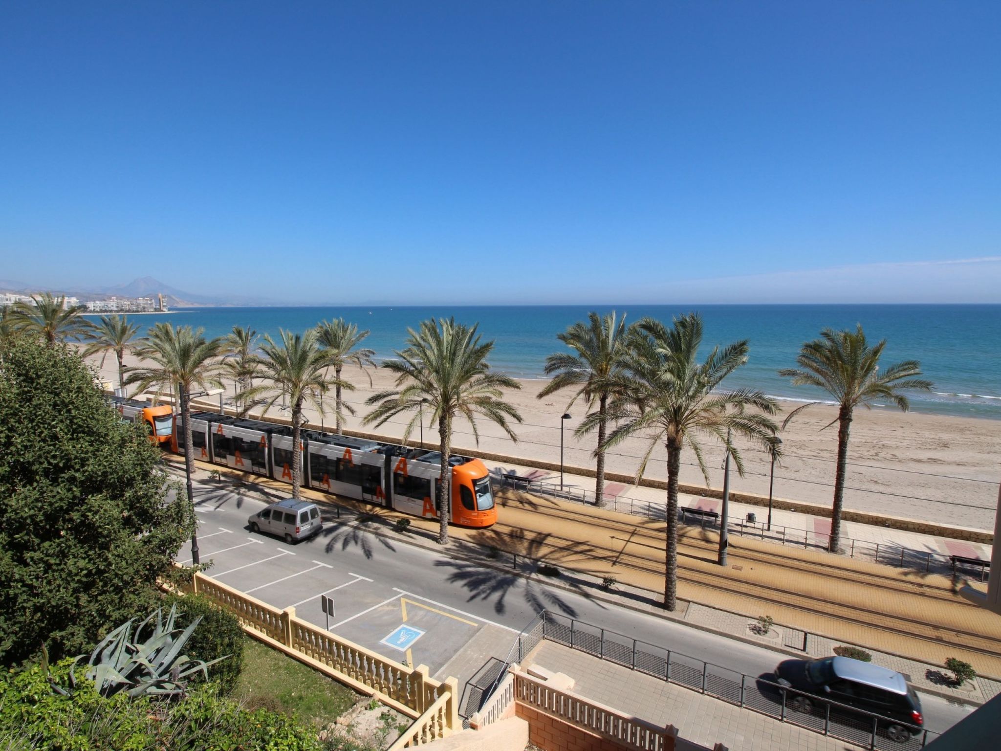 A coastal road with palm trees, a beach, and a clear blue sky.