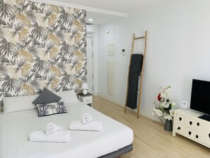 A hotel room with a bed, a TV, a wardrobe, a towel rack, and a wall with a tropical leaf pattern. - APARTAMENTO SOL Y LUZ 2 by Interhome (El Campello/Villajoyosa)