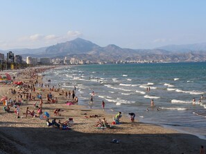 A beach with people sunbathing and swimming, a city skyline in the background, and mountains. - APARTAMENTO SOL Y LUZ 2 by Interhome (El Campello/Villajoyosa)