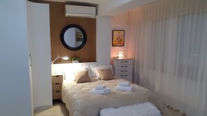 A bedroom with a bed, a bedside table, a lamp, a mirror, and a window with curtains. - ESTUDIO PLAYA POSTIGUET by Interhome (Alicante)