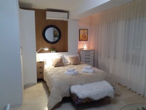 Ein Schlafzimmer mit einem Bett, einem Nachttisch, einer Lampe, einem Spiegel und einem Fenster mit Vorhängen.