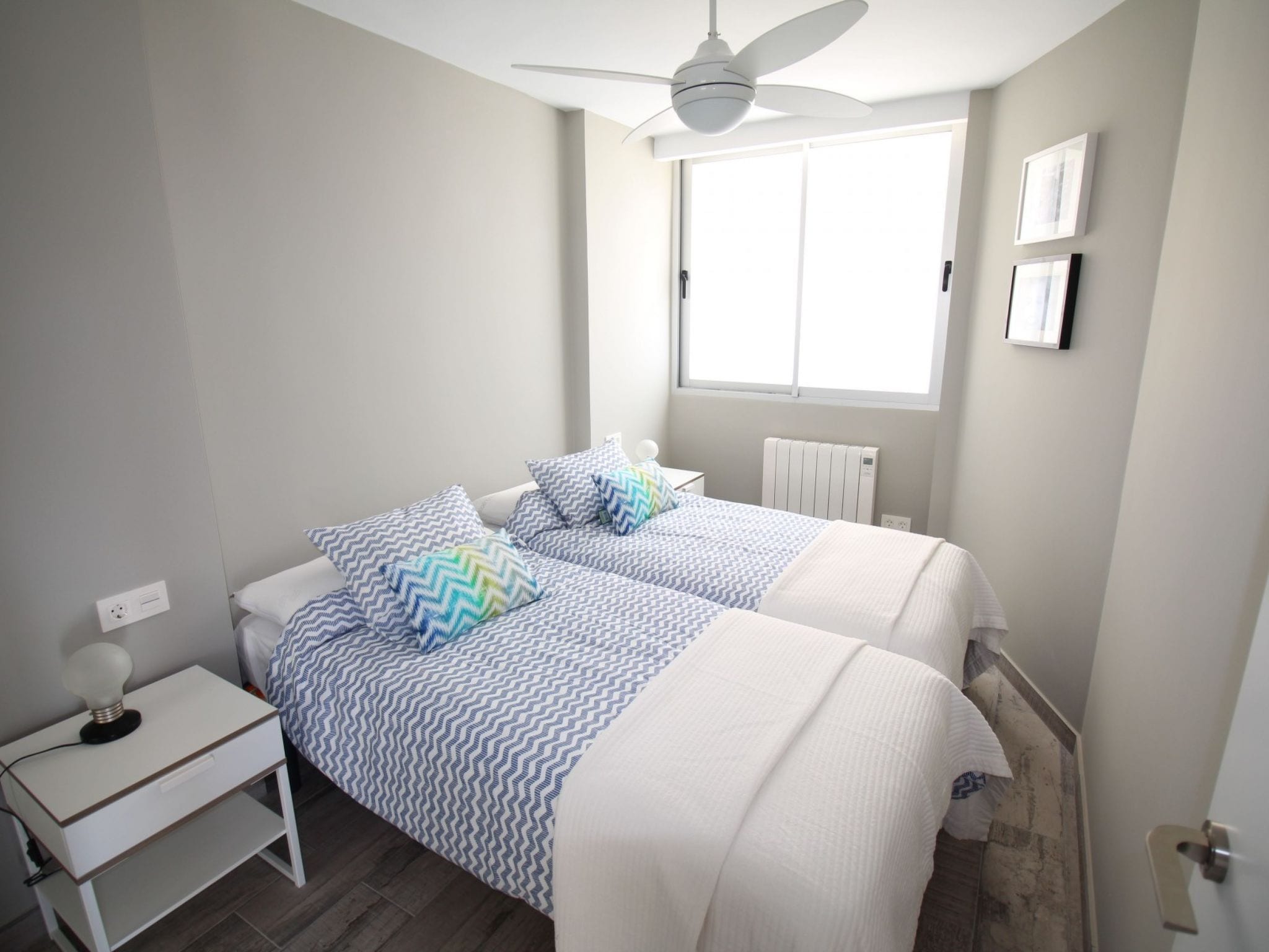 A bedroom with two beds, a ceiling fan, a window, and a radiator.
