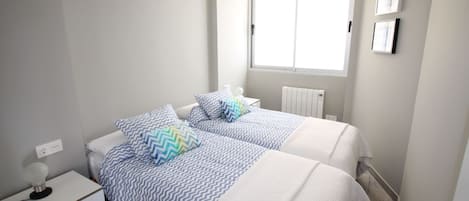 A bedroom with two beds, a ceiling fan, a window, and a radiator.