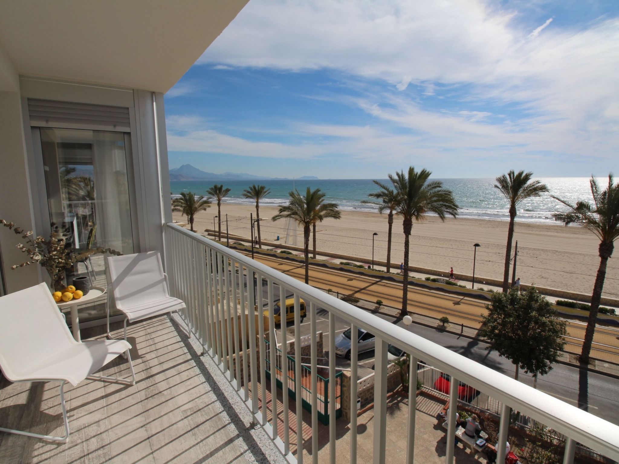 A balcony with a view of a beach, palm trees, and a distant mountain.