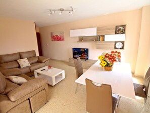 A living room with a sofa, coffee table, TV, and a dining area with a table and chairs. - APARTAMENTO LAS TORRES by Interhome (El Campello/Villajoyosa)