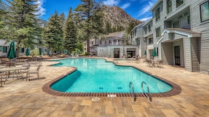 A pool with a mountain backdrop, outdoor seating, and a building with multiple windows. - Mountainside at Palisades Tahoe Lodge (Olympic Valley)