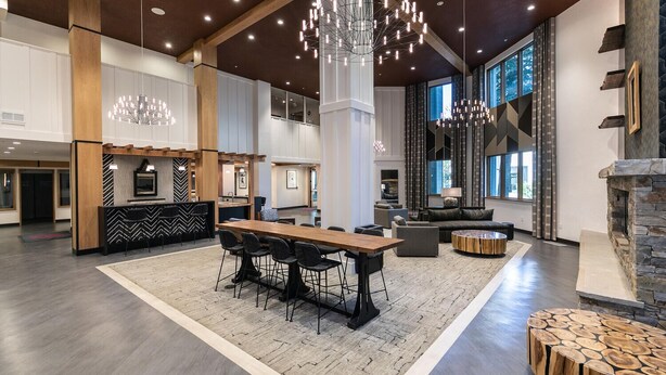 A spacious lobby with a central dining area, a fireplace, and modern lighting fixtures. - Mountainside at Palisades Tahoe Lodge (Olympic Valley)