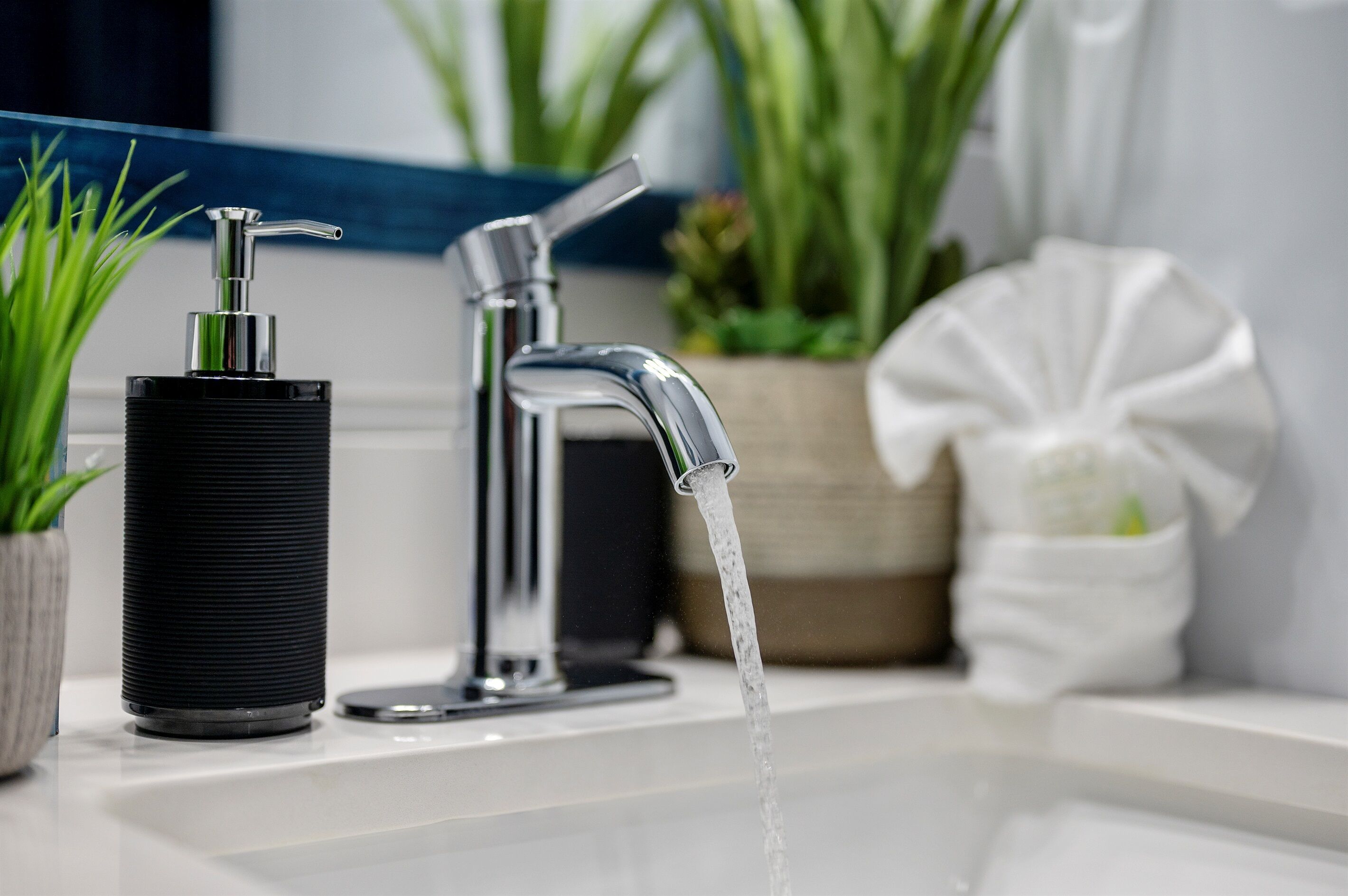 A bathroom with a modern faucet, a black soap dispenser, and a white towel holder.