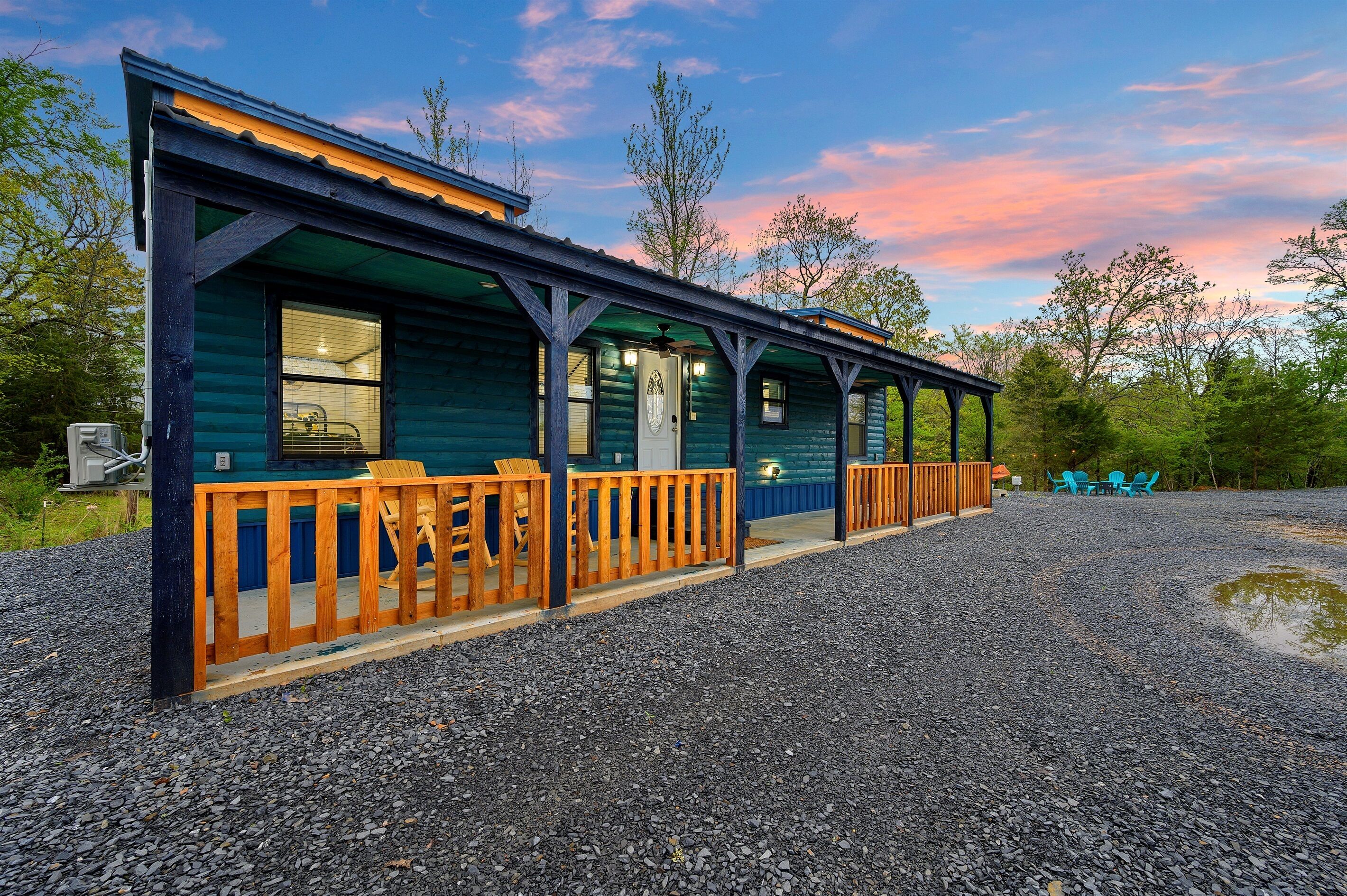 A rustic cabin with a porch, wooden railings, and a gravel driveway.