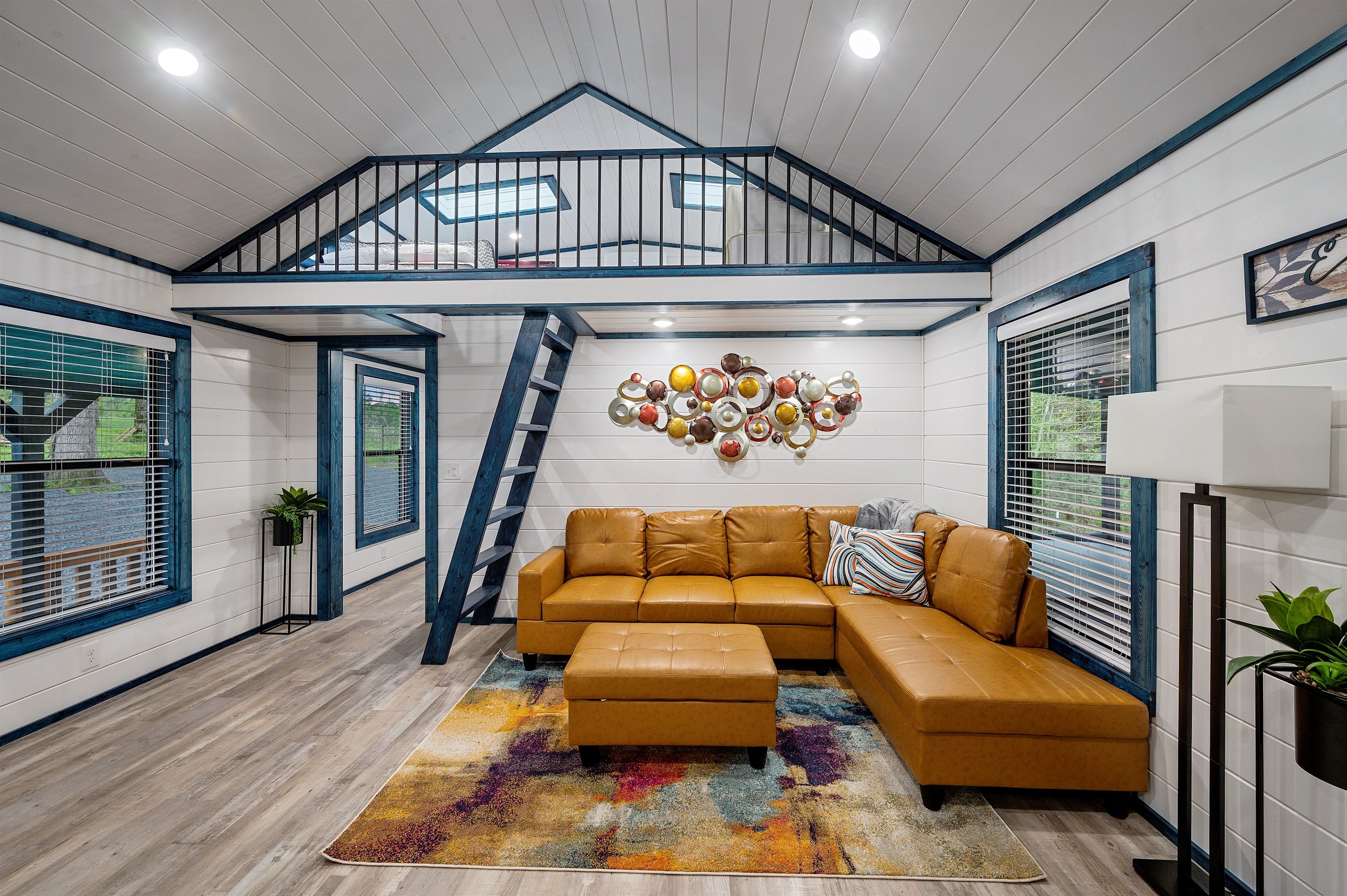 Una sala moderna con un sofá modular, una alfombra colorida, un elemento decorativo en la pared y una escalera que sube a un nivel superior.