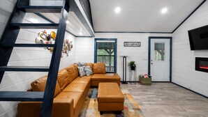 Un salon moderne avec un canapé d’angle, un escalier, un téléviseur à écran plat et une porte avec une fenêtre.