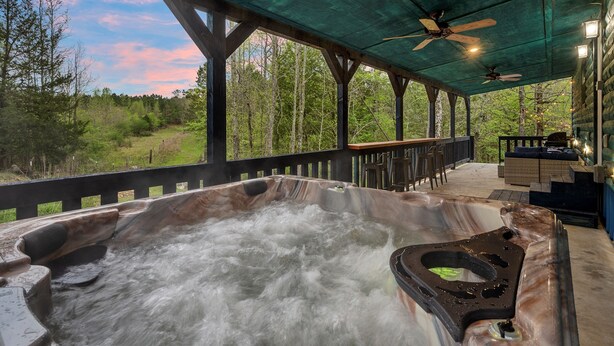 Un bain à remous agrémenté d’une cascade, une terrasse couverte avec des sièges et une vue sur la forêt environnante.