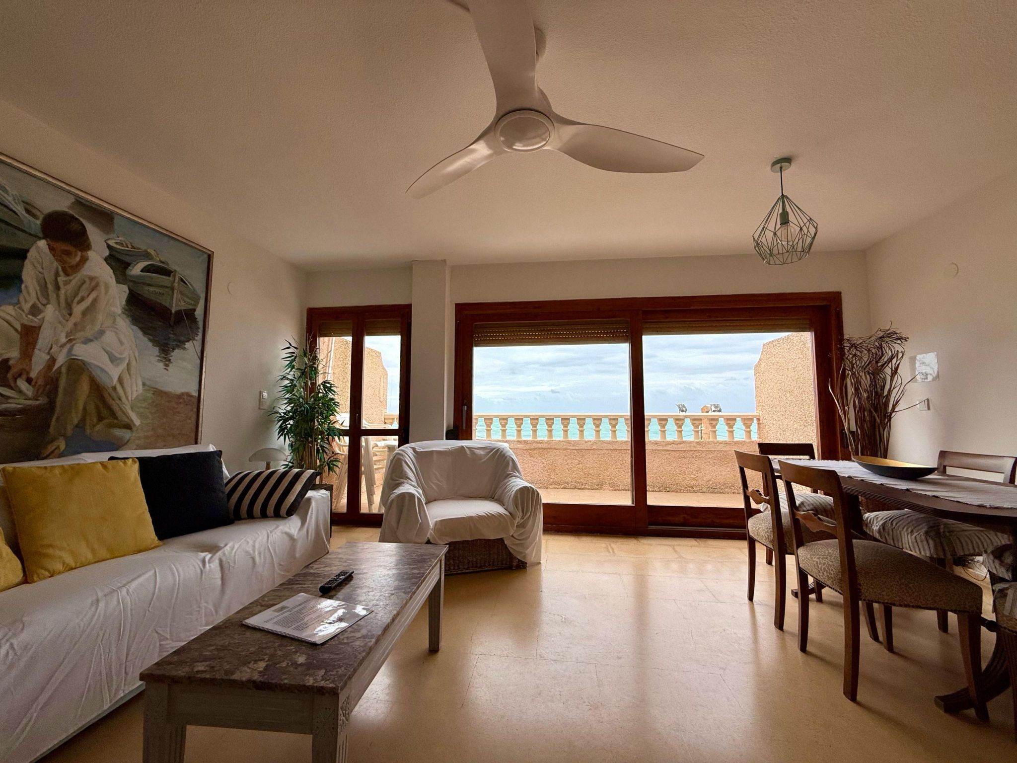 A living room with a sofa, armchair, dining table, and a ceiling fan.