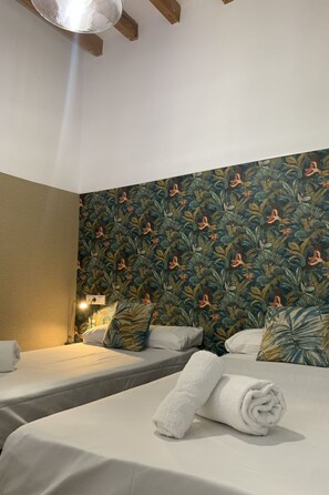 Una habitación de hotel con dos camas, una mesita de noche y una pared con un diseño de hojas tropicales.