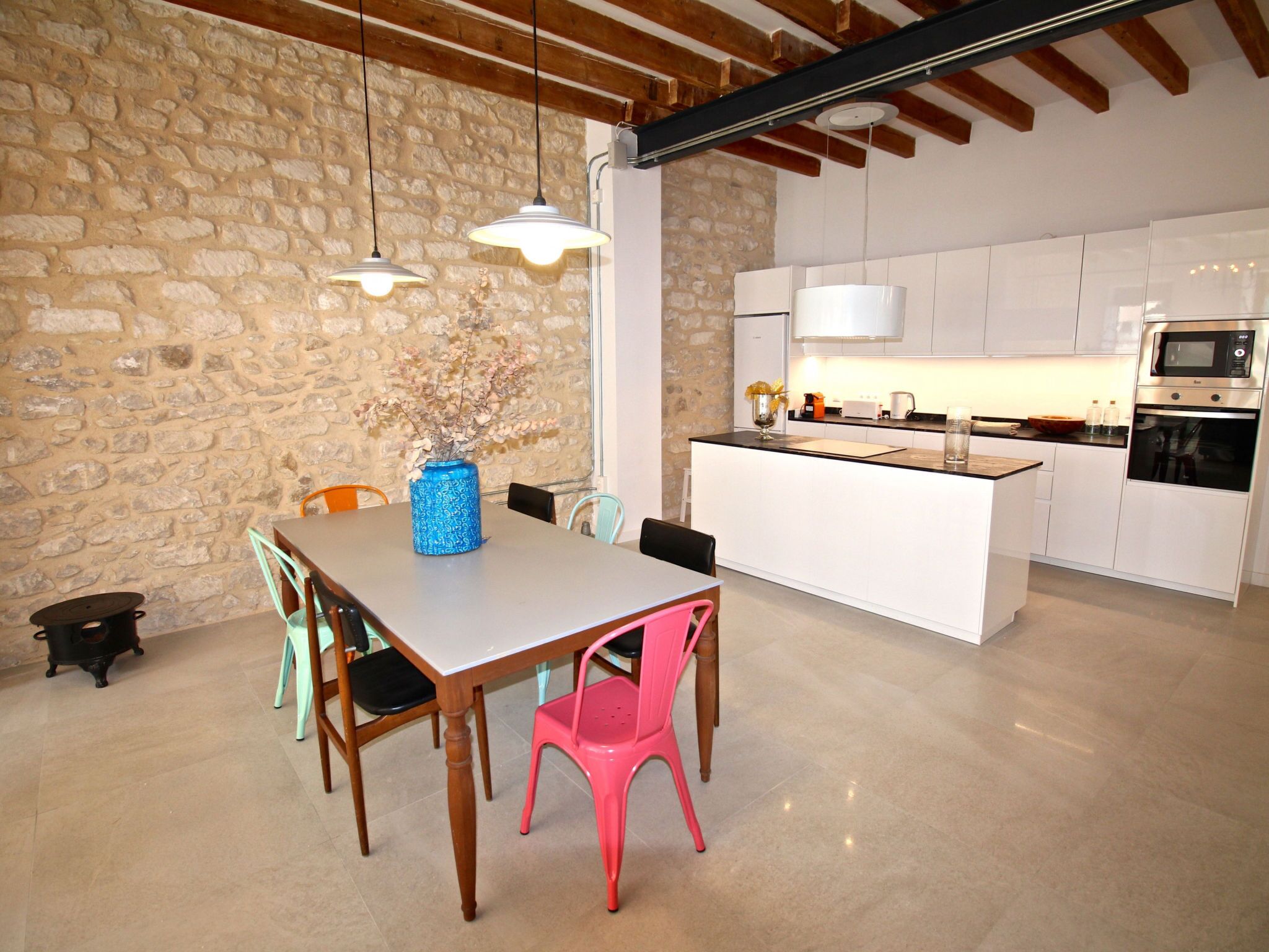A modern kitchen with white cabinets, a built-in oven, and a dining area with a wooden table and chairs.