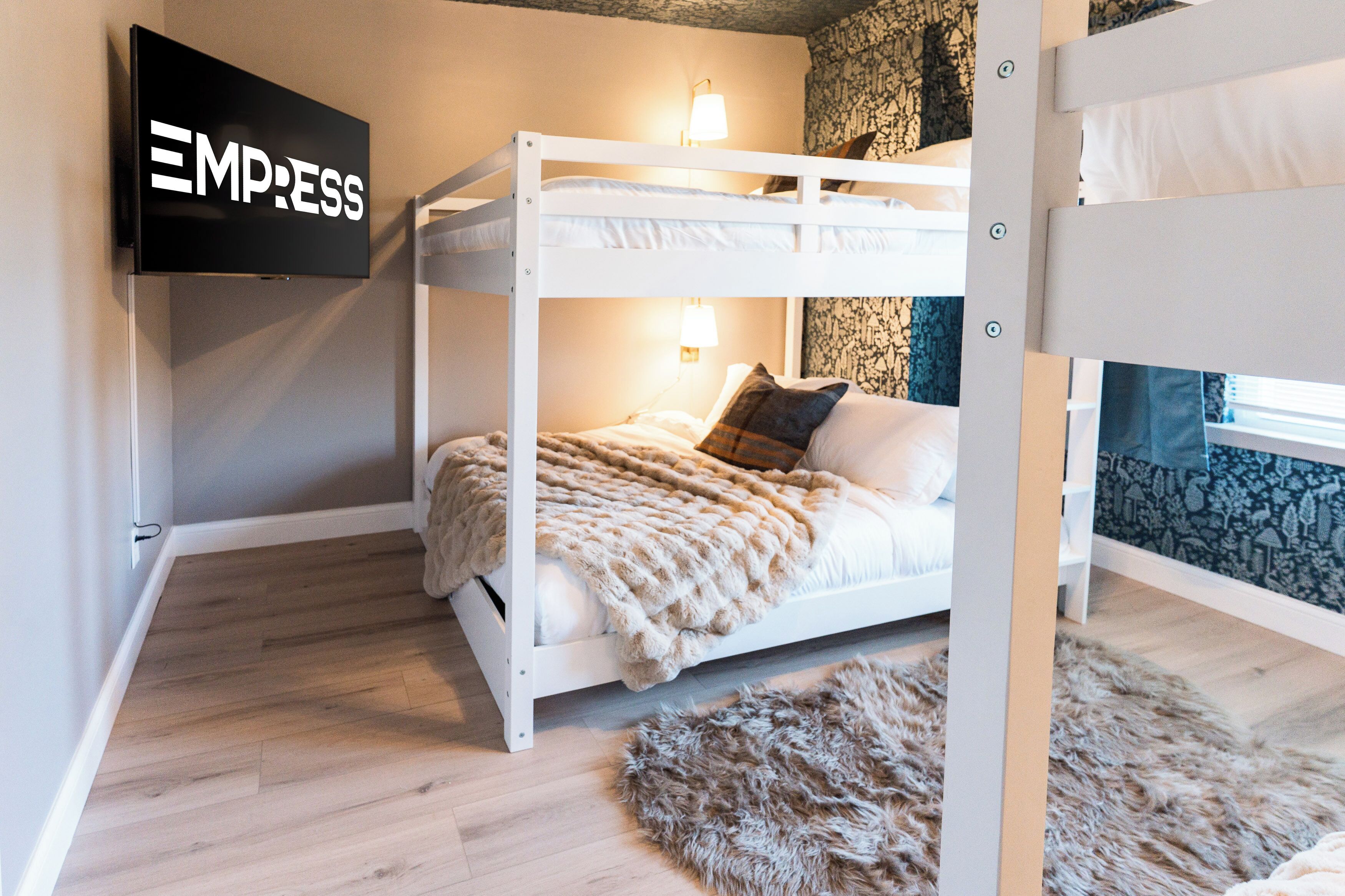 A bunk bed room with a television on the wall, a fluffy rug, and a patterned wall.