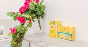 Eine transparente Glasvase mit rosa Blumen auf einer weißen Oberfläche, neben zwei Packungen Lipton Tee.