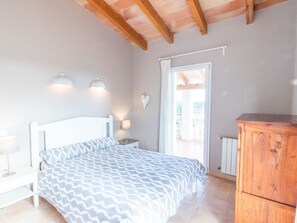 Ein Schlafzimmer mit einem Bett, Nachttischlampen, einer Holzkommode und Blick ins Freie.