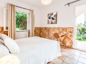 Une chambre à coucher avec un lit, un mur en pierre, une fenêtre avec des rideaux et un tableau accroché au mur.
