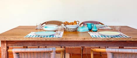 Una mesa de madera con platos azules y blancos, una cesta de pan y una botella verde.
