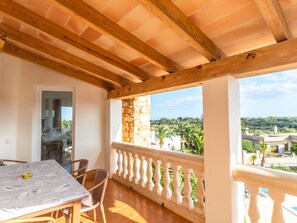 Ein überdachter Außenbereich mit Holzbalkendecke, ein Balkon mit weißer Brüstung und Blick auf eine grüne Landschaft.