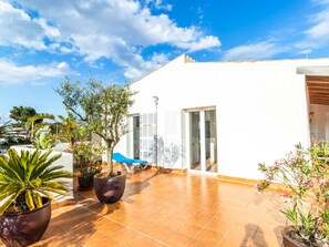 Une maison moderne dotée d’un patio carrelé, de plantes en pot et d’un fauteuil de salon bleu.
