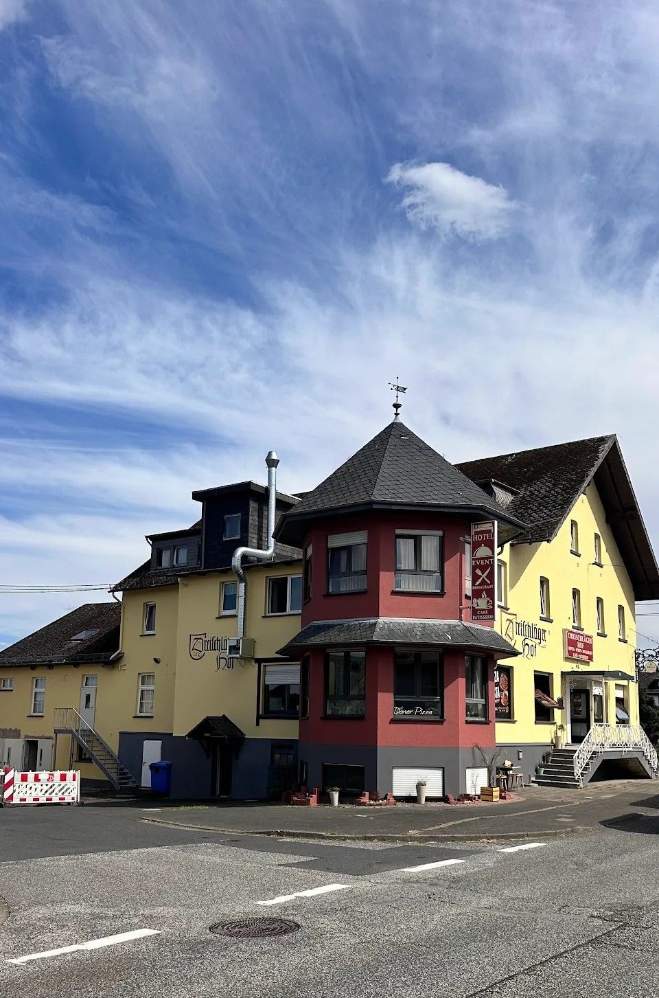 Ein mehrstöckiges Gebäude mit einer roten und gelben Fassade, einer Wetterfahne und Schildern, die ein Hotel, ein Restaurant und ein Café kennzeichnen.
