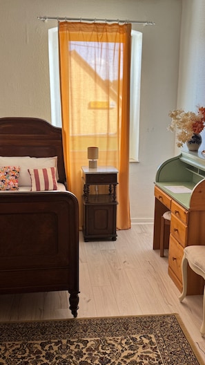 Une chambre à coucher avec un lit, une table de chevet, un bureau, une chaise et une fenêtre avec des rideaux.